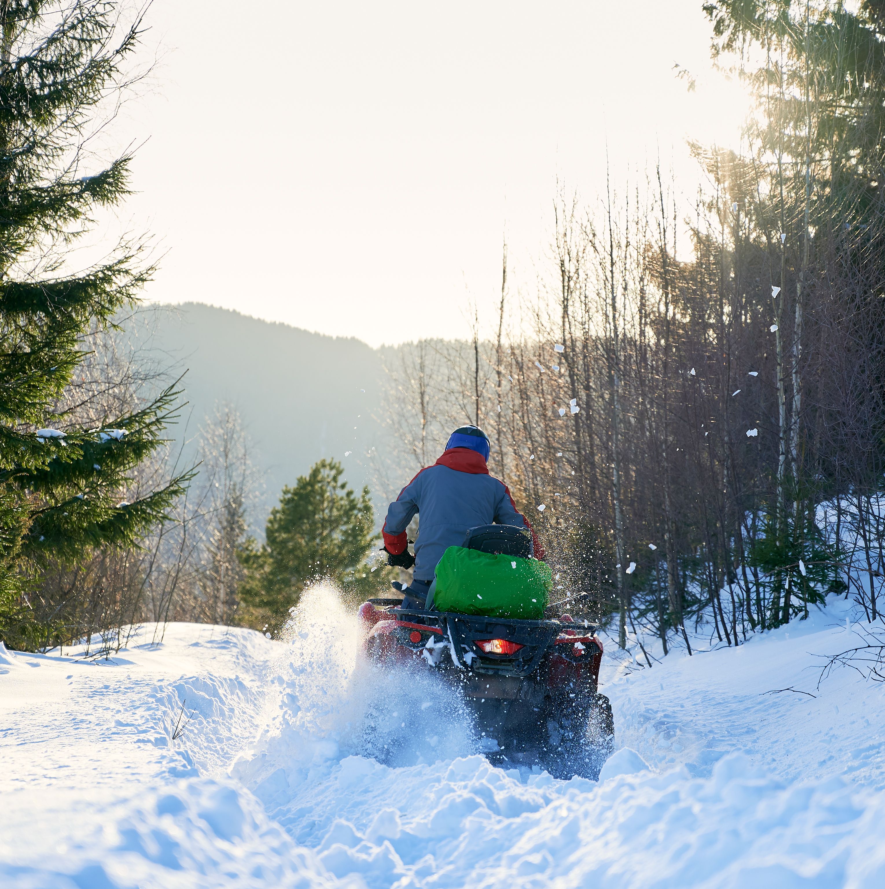 Vue arrière d’un conducteur pilotant un quad VTT en montagne durant l’hiver