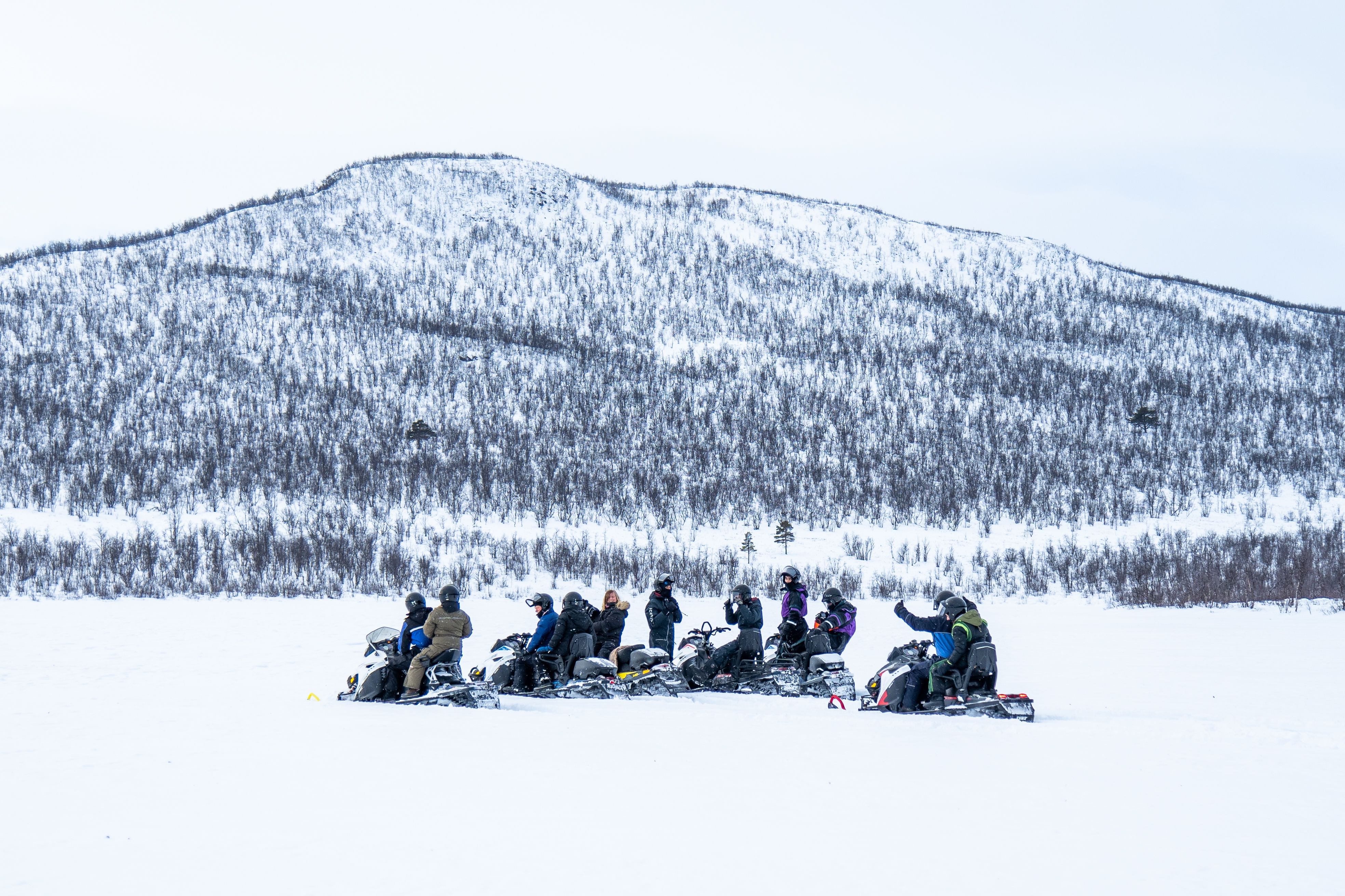 Groupe de personnes faisant de la motoneige dans un paysage montagneux enneigé