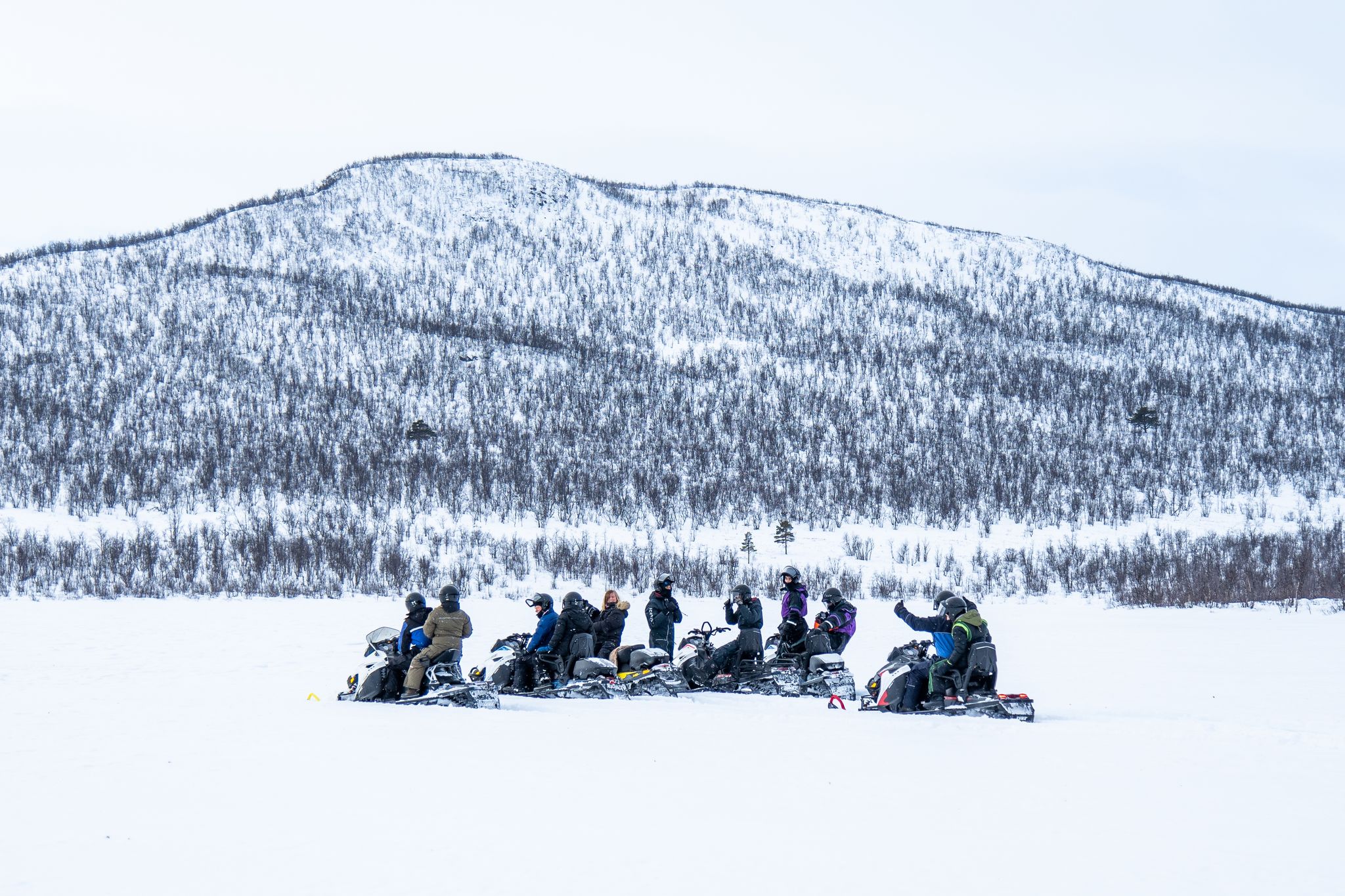 Groupe de personnes faisant de la motoneige dans un paysage montagneux enneigé